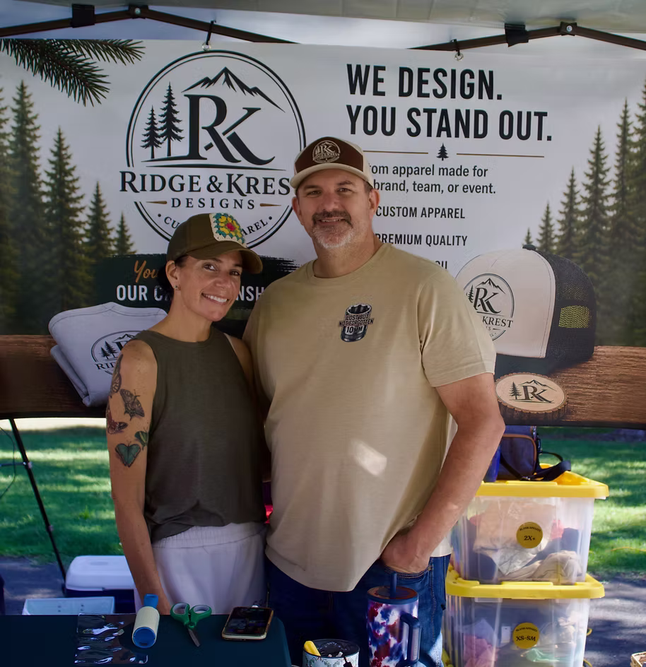 Ridge & Krest Designs founders standing together outdoors in Oregon, representing the people and personal craftsmanship behind the custom apparel studio